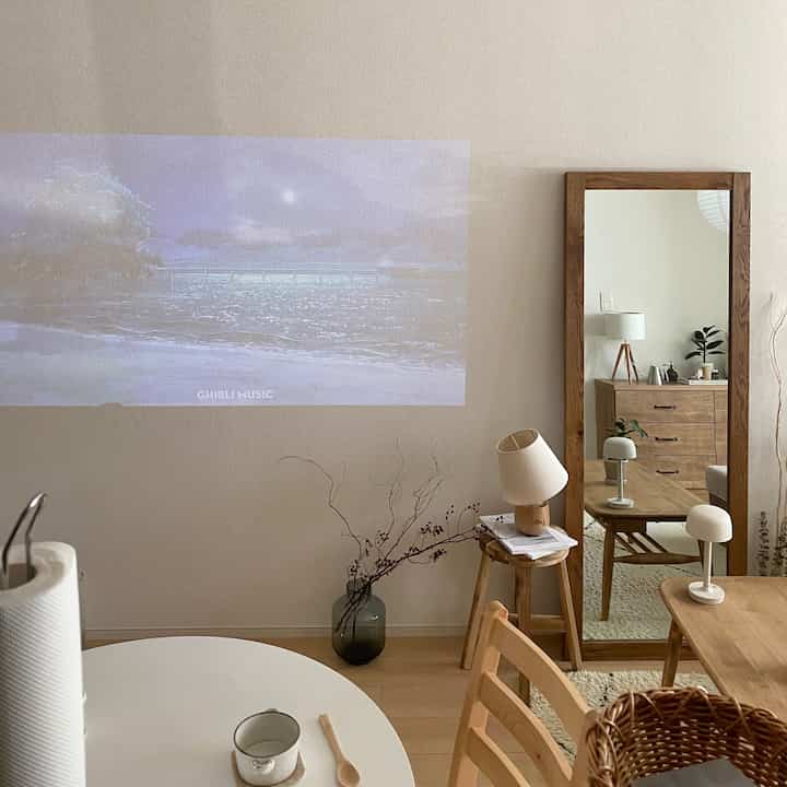 Natural tone kitchen and living space featuring wooden furniture, large mirror, and projector screen on the wall, creating a cozy interior