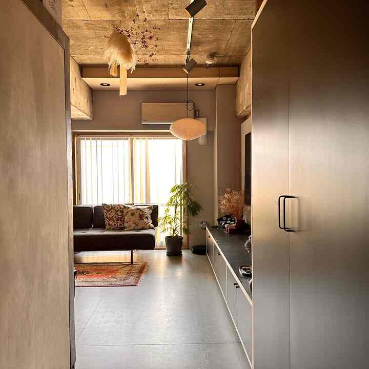 温かみのあるベージュとダークグレーの色調のリビング、ハーマンソファとプランターが配置された自然でくつろげる雰囲気のインテリア