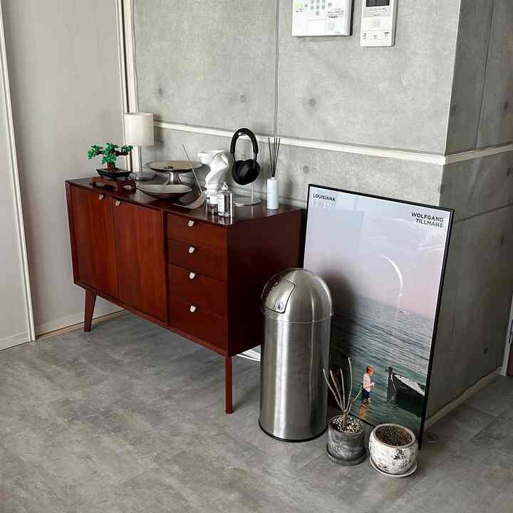 グレー色調の玄関スペース、濃い茶色のキャビネットと金属製ゴミ箱が配置されたモダンな雰囲気のインテリア