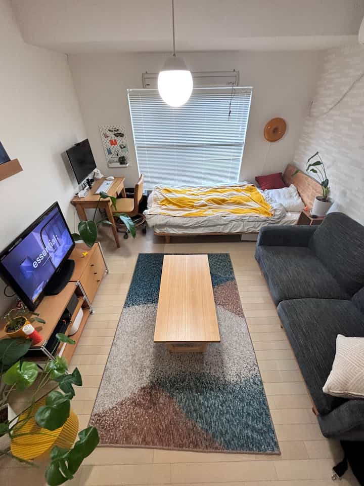 White-toned room with a bed featuring yellow blanket, dark gray sofa, and wooden coffee table in a natural-style single household bedroom
