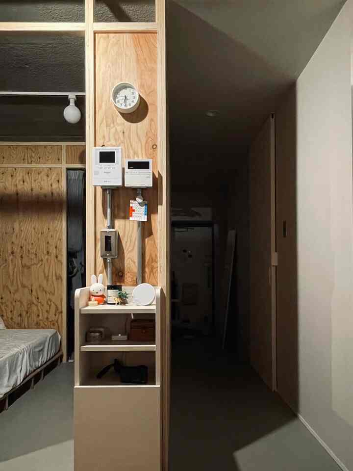 ナチュラルなブラウン調のワンルーム、合板の壁と白いベッドが配置されたミニマルな空間