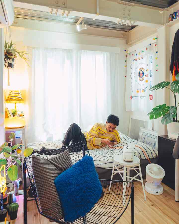 白いカーテンとナチュラルな床のある小さな一人暮らしの寝室、ベッドとアームチェアが配置された居心地の良い空間