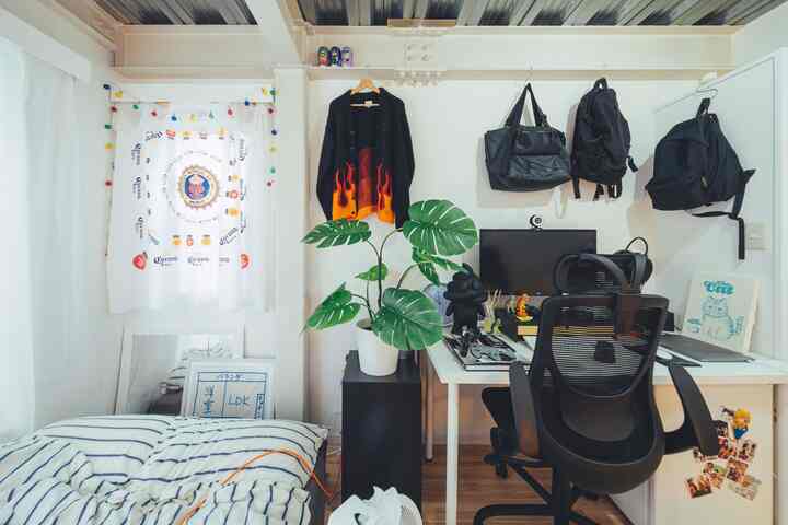 白い壁と黒い家具が特徴的な6畳のホームオフィス、机とオフィスチェア、モンステラのフェイク植木が配置された清潔感のある空間