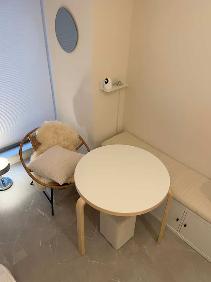 白とベージュのトーンでまとめられた狭いダイニングコーナー、ラウンドテーブルとラタンのアームチェアが配置されたシンプルでモダンな空間