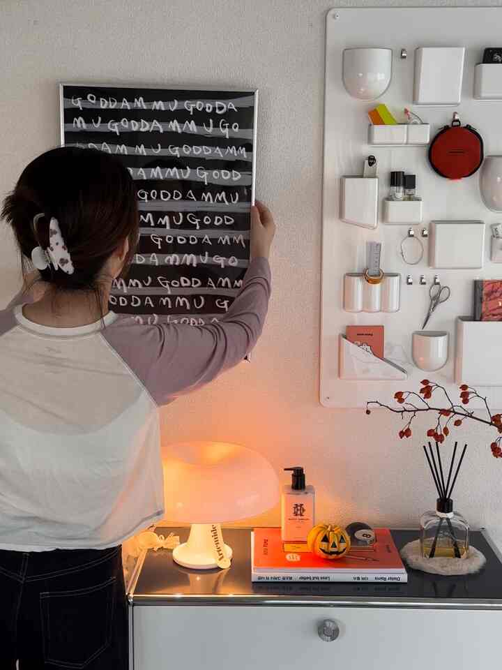 ホワイトとオレンジの色調が調和するサイドボード上の小物と壁掛け収納が配置されたミニマルなホームギャラリー空間