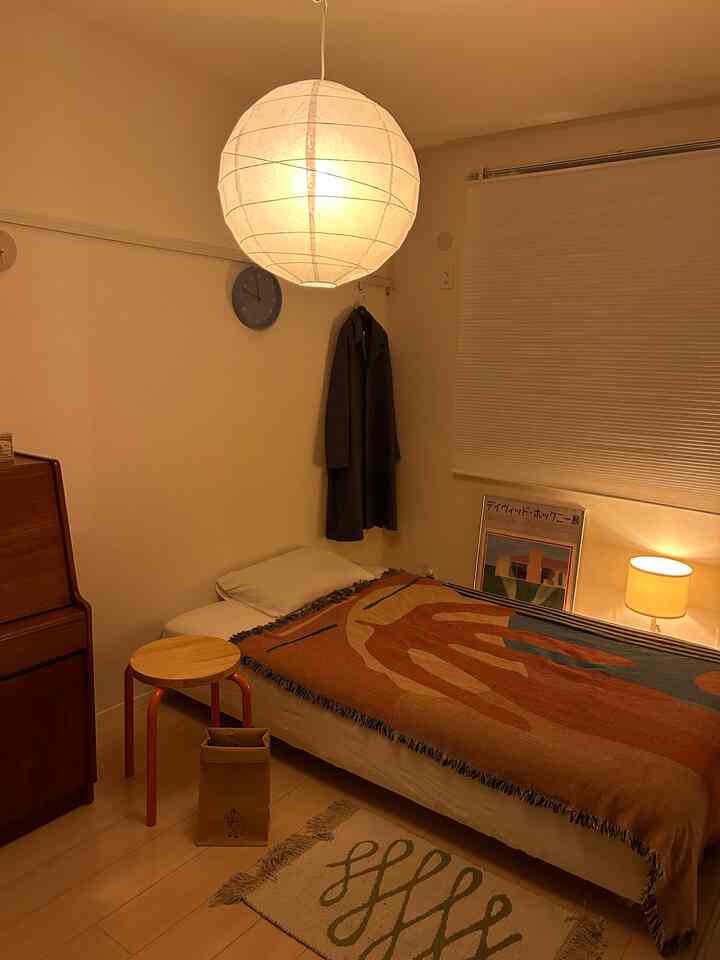 暖かい黄色の照明が灯るナチュラルでモダンな寝室、ベッドと木製のスツールが配置された印象的な空間