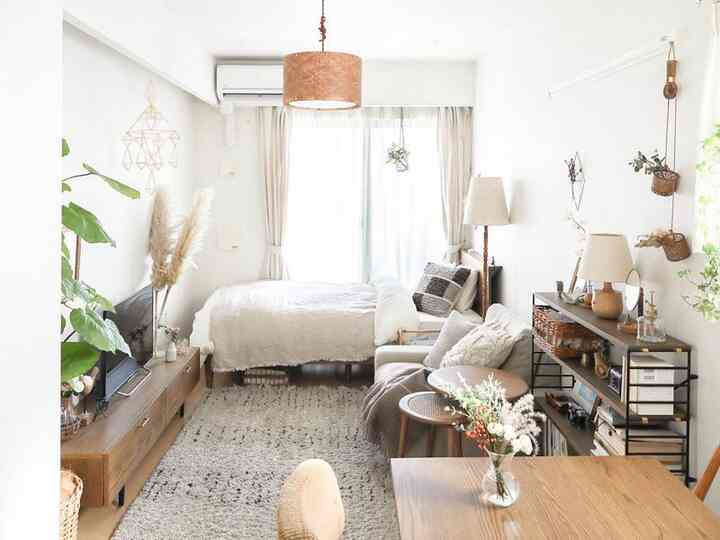 Bright natural-tone studio apartment bedroom featuring wooden furniture and plants for a cozy atmosphere