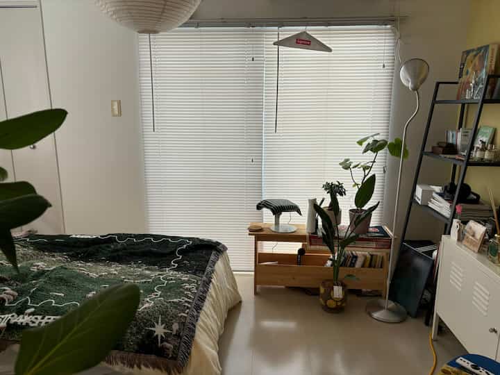 ナチュラルな木目調とグリーンの植物が配置された6畳の寝室、落ち着いたレイアウトの印象的な空間