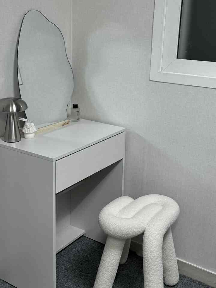 グレーとホワイトのトーンのワンルーム、非定形鏡とホワイトスツールが置かれたシンプルな化粧台のインテリア