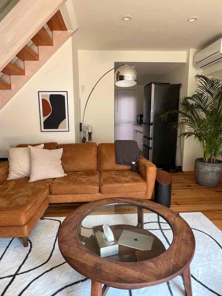 温かみのあるウッドトーンの床とブラウンソファが配置されたナチュラルモダンなリビング、アレカヤシの植物とアーチ型フロアランプのある雰囲気のあるインテリア