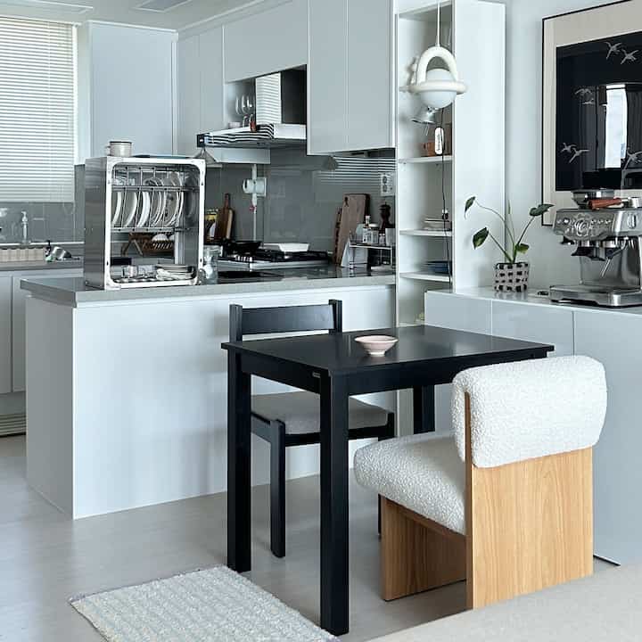 White modern kitchen and dining space featuring wooden chairs and coffee machine with a clean, calm atmosphere
