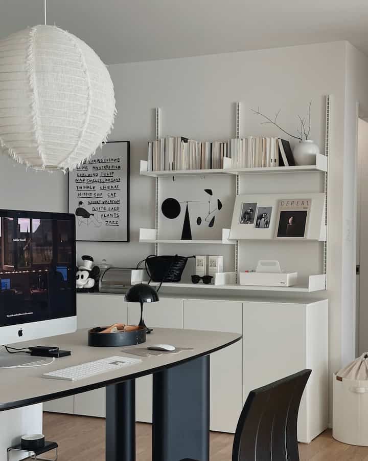 Modern white and black toned home office featuring a desk, bookshelves, and wall shelves with a minimalistic atmosphere
