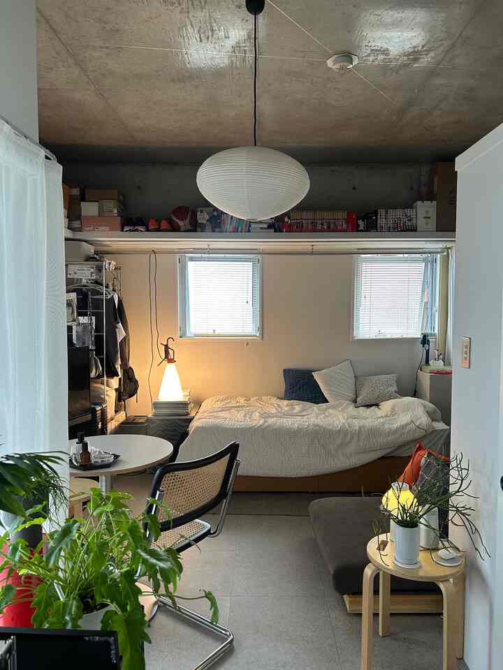 白と茶色のトーンでまとめられたワンルーム寝室兼リビング、ベッドとソファが配置された居心地の良いインダストリアルスタイルの空間