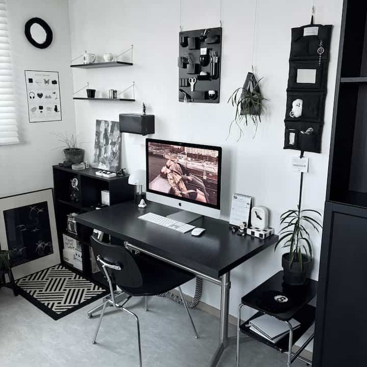 Monotone home office desk space featuring a black desk and chair, wall shelves, and accessories arranged in a clean, cohesive design