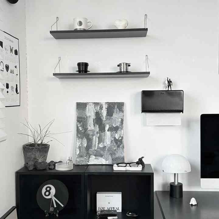 Monotone black and white home office featuring a DULTON tissue case mounted on wall, floating shelves, desk lamp, and decorative items arranged neatly
