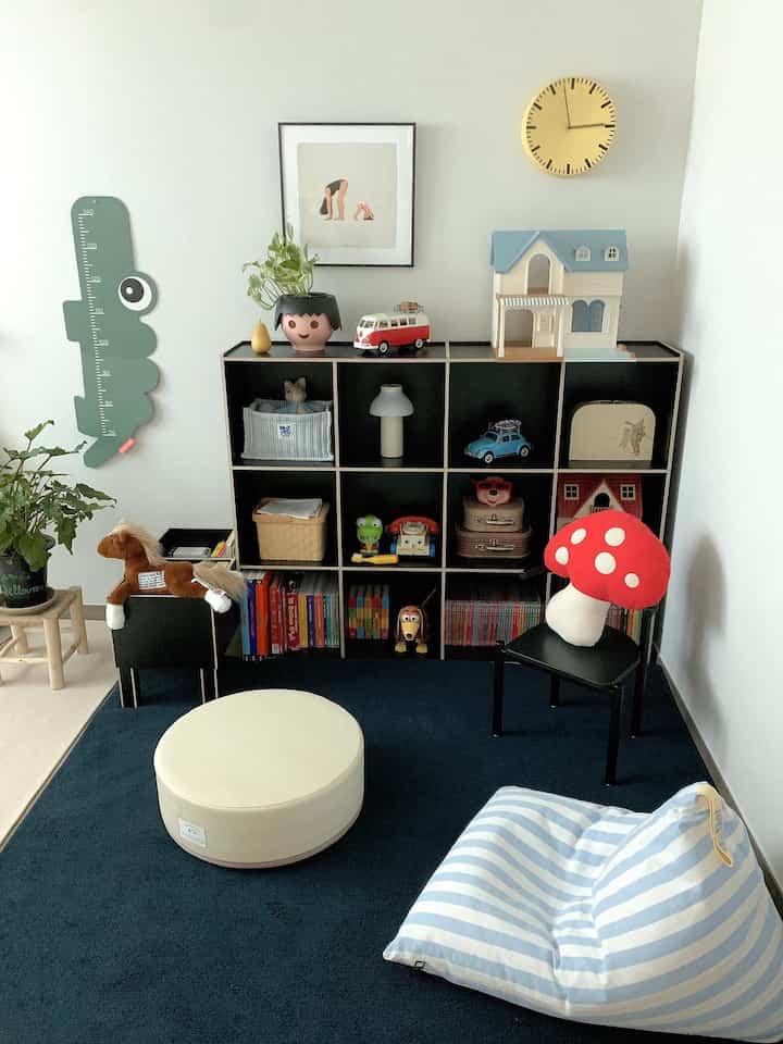 白い壁とダークネイビーのラグが敷かれた子供部屋、黒い本棚におもちゃやクッションが配置された雰囲気のあるインテリア