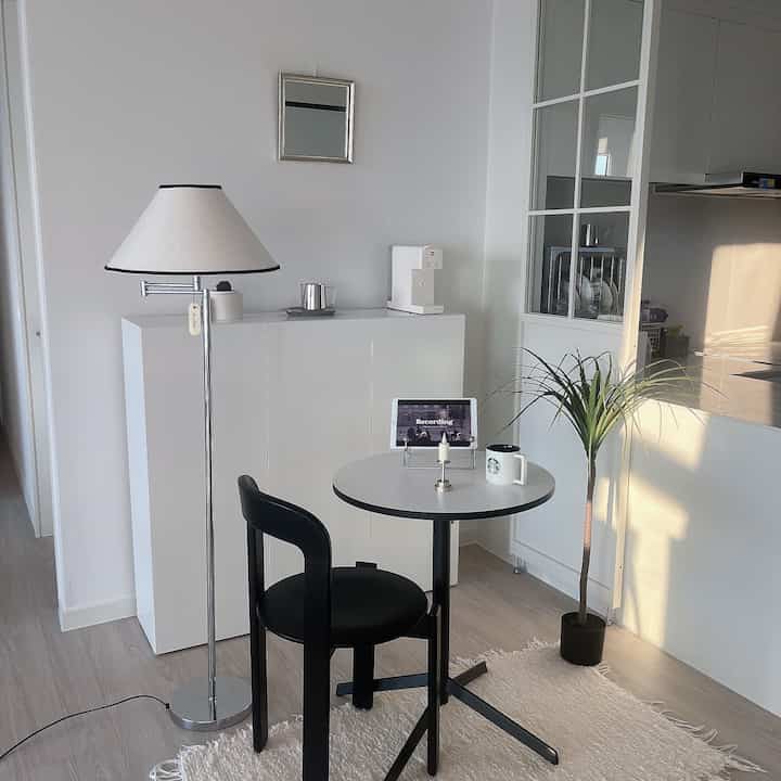 ホワイトとブラックの色調でまとめられた一人暮らし用のコンパクトな部屋、フロアランプとダイニングチェアが配置されたおうちカフェのあるインテリア