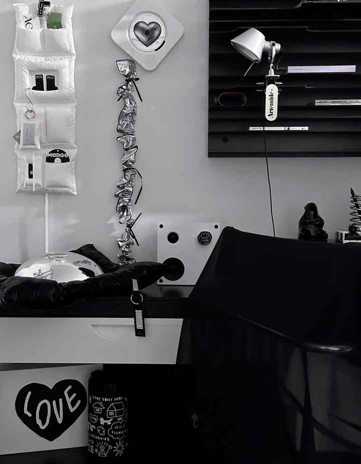 Modern monotone home office featuring a white desk, black chair, wall sconce, and shelf with a sleek interior design