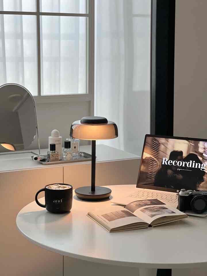 Bright living space with white round table featuring black table lamp, coffee mug, laptop, and an open book