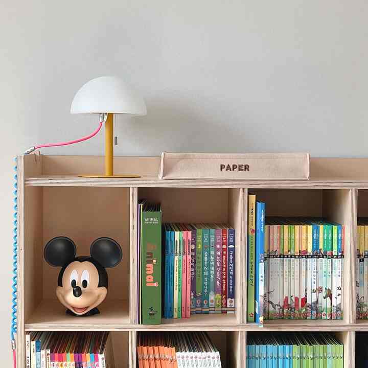 ベージュ色調の子供部屋、全面本棚とテーブルランプが配置された温かみのあるインテリア