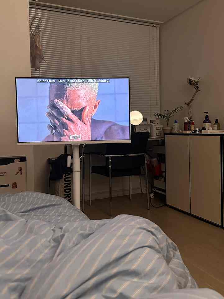 ブラックとホワイトの色調の寝室、中央にテレビモニターとデスク、青のストライプ寝具が配置された雰囲気のあるインテリア