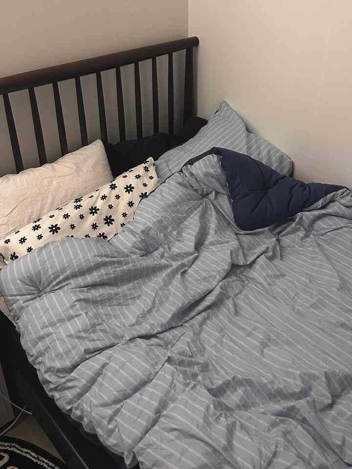 ネイビーとブルーのストライプ寝具が配置されたコンパクトな寝室で、ミッドセンチュリーモダンの木製ベッドフレームが印象的な空間