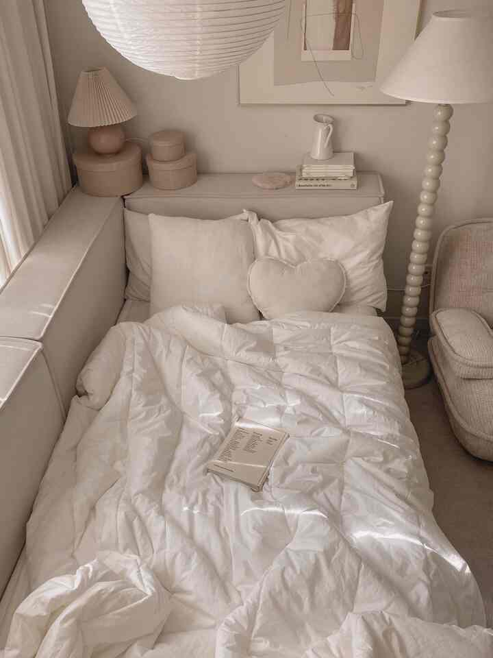 柔らかなホワイトとベージュの色調の寝室、白いベッドとクッション、フロアランプが配置された雰囲気のあるインテリア