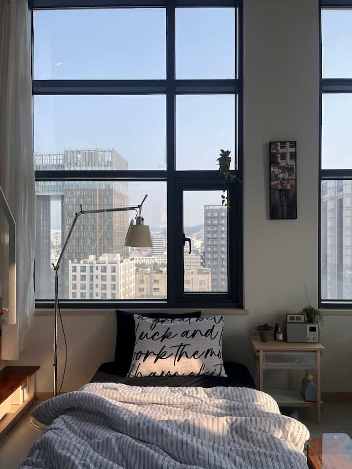 Monotone white and black studio bedroom featuring large windows and striped duvet cover with cozy atmosphere