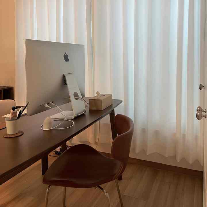 Warm wood tone home office with white curtains, minimalist desk and chair arranged for a cozy atmosphere