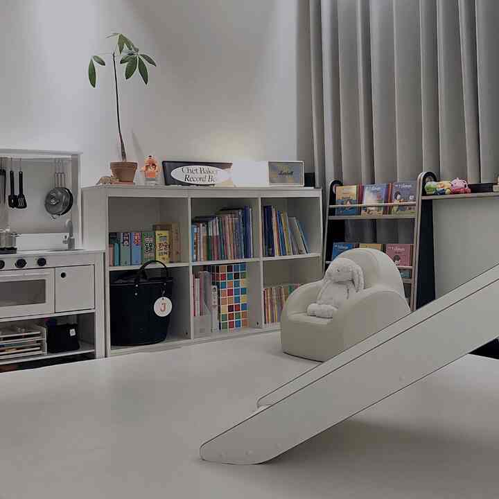 ホワイトとグレーのトーンのリビング、絵本棚や滑り台、子供用ソファが配置された清潔感のあるインテリア