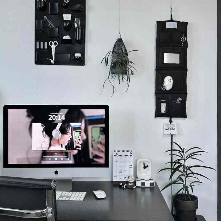 Monotone home office space in white and black, featuring an iMac on desk with organized wall storage in a compact workspace