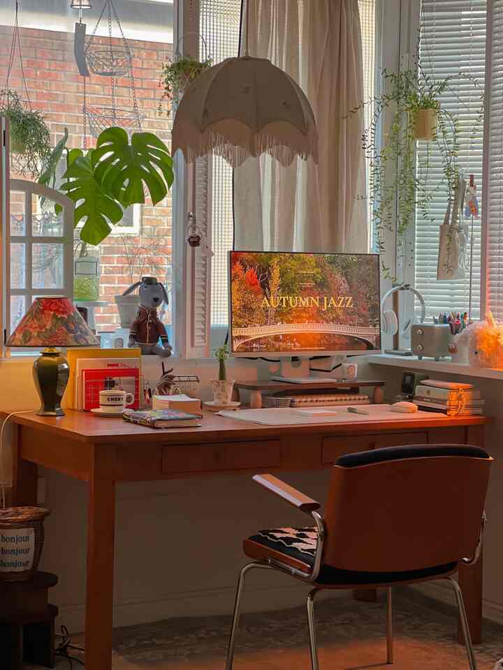 暖かい木の色調と秋の雰囲気があるホームオフィスのデスク空間、植物とヴィンテージ照明が配された居心地の良い作業室