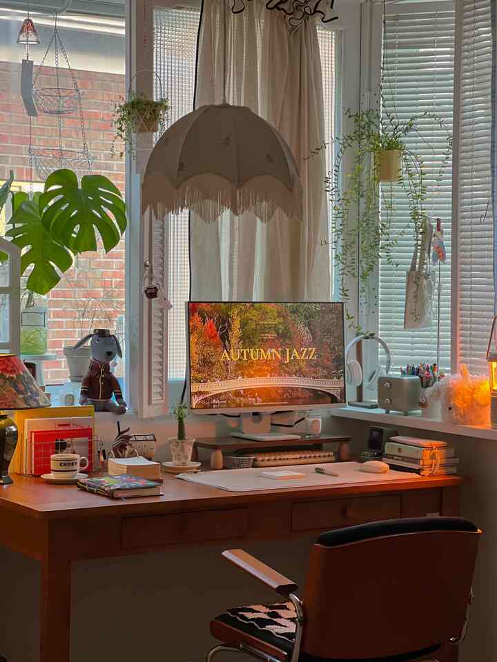 ナチュラルモダンな窓際のホームオフィス、木製デスクとオフィスチェアが配置され、照明と植物が調和した印象的な空間