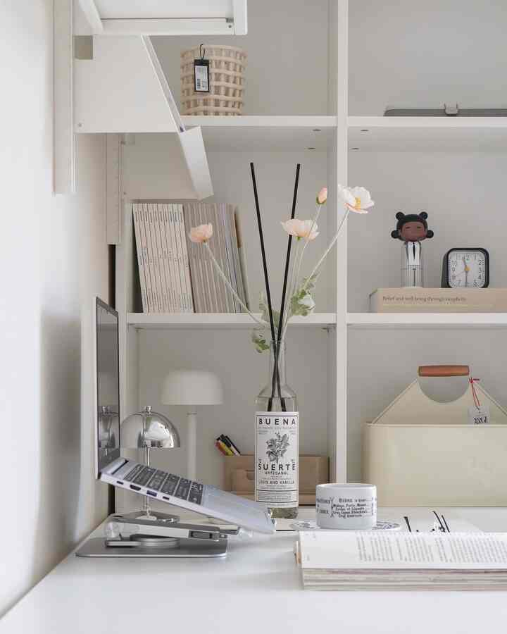White-toned home office space featuring a desk and bookshelf arranged in a minimalistic style