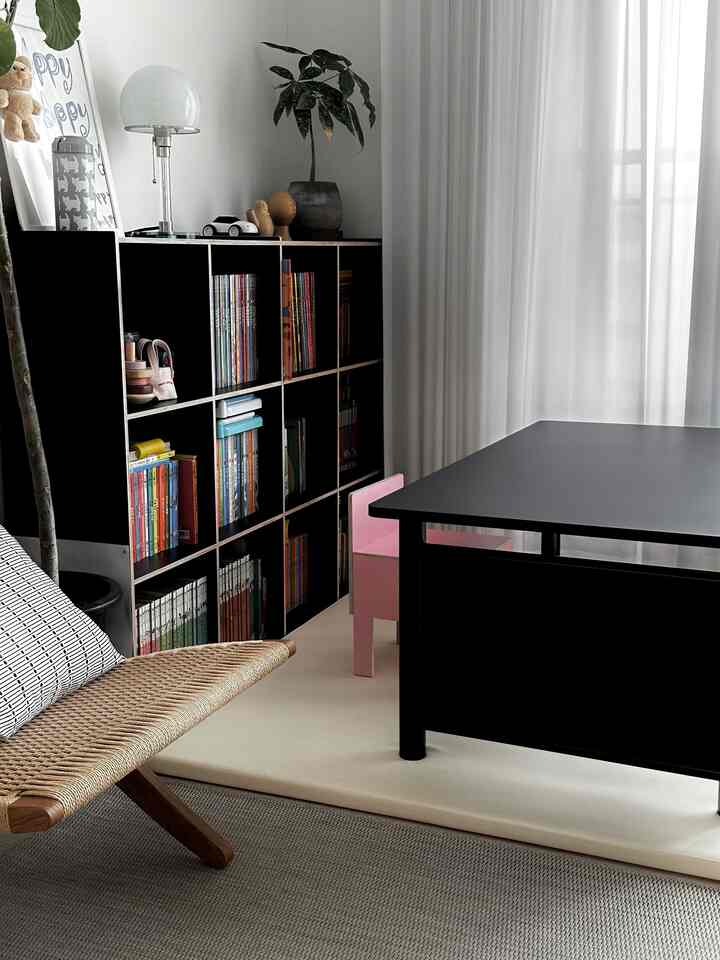A modern kids' room in black and white tones featuring a black bookshelf, desk, and a small pink chair with bright natural light