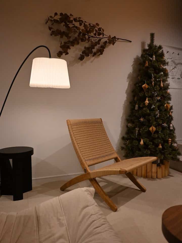 ナチュラルカラーと木目調のコンパクトなリビング、ハーフクリスマスツリーと編み込みラウンジチェアが配置された雰囲気のある空間
