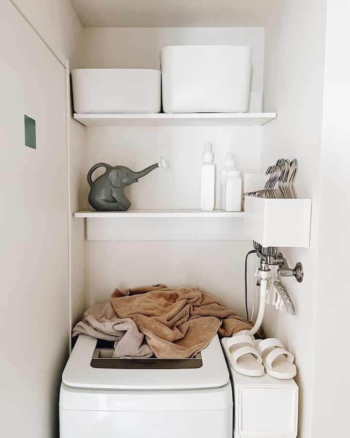 ホワイトとベージュのトーンが映える、厚手のタオルと整理された棚があるミニマルなランドリールーム