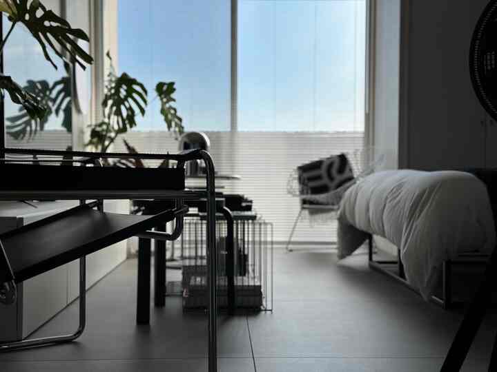 白とグレーのトーンでまとめられた小さなモダンな寝室、デスクとモダンなアームチェアが配置されたシンプルな空間