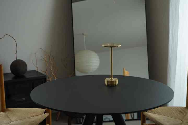 ゴールドのテーブルランプが置かれた黒い丸テーブルと木製チェアのモダンでシンプルなダイニングルーム