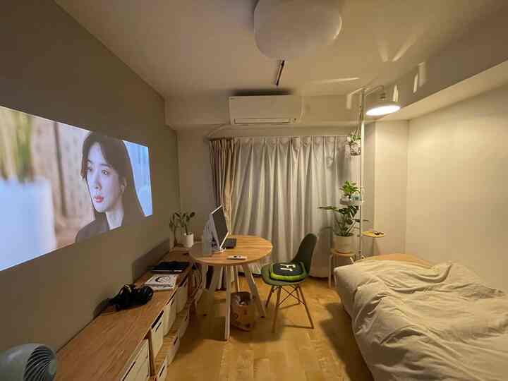 白と木目調の調和が感じられる5.5畳の1Kワンルーム、ベッドと小さな丸テーブルのワークスペースが配置された雰囲気のある空間