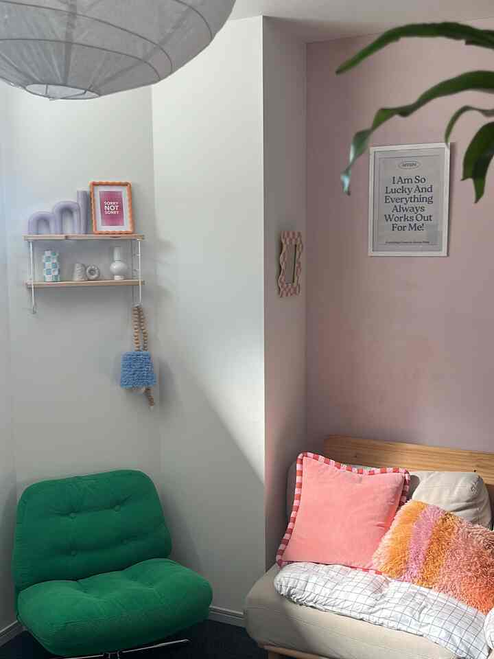 ピンクの壁と木目調のソファ、緑のアームチェアが配置された居心地の良いリビングスペース