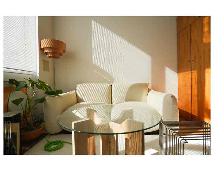 Modern living room with beige sofa and transparent glass table, featuring wood tones and natural sunlight