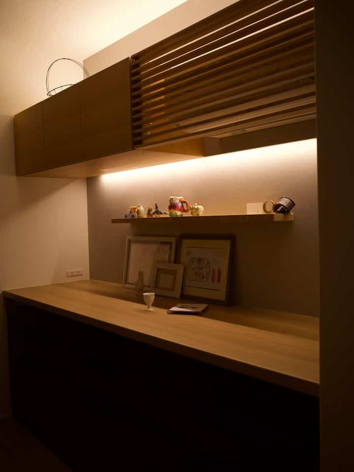 A cozy kitchen space with beige walls and natural wood-tone storage cabinets illuminated by warm lighting, featuring neatly arranged decorative objets.