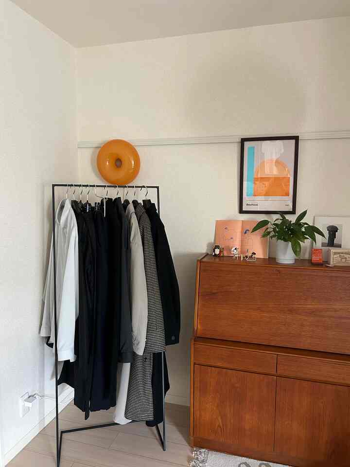 白い壁と床に、ブラックのアイアンハンガーラックとブラウンのヴィンテージ風ライティングビューローが配置されたシンプルなミッドセンチュリーモダンな空間