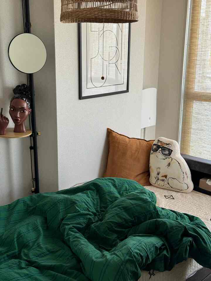 ベージュの壁と緑の掛け布団カバーがある寝室、猫クッションや様々な小物が配置された雰囲気のあるインテリア