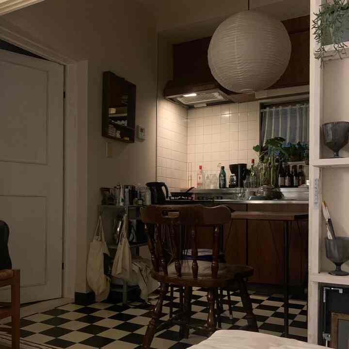 白と黒のチェック柄の床、木目調のキッチン家具とダイニングチェアが配置されたアパートのキッチンスペース