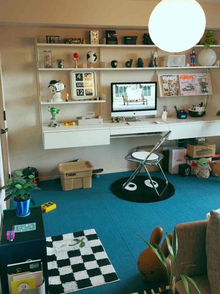 Blue carpeted home office with white wall shelves and desk, featuring a black chair and various decorations in a cozy setting