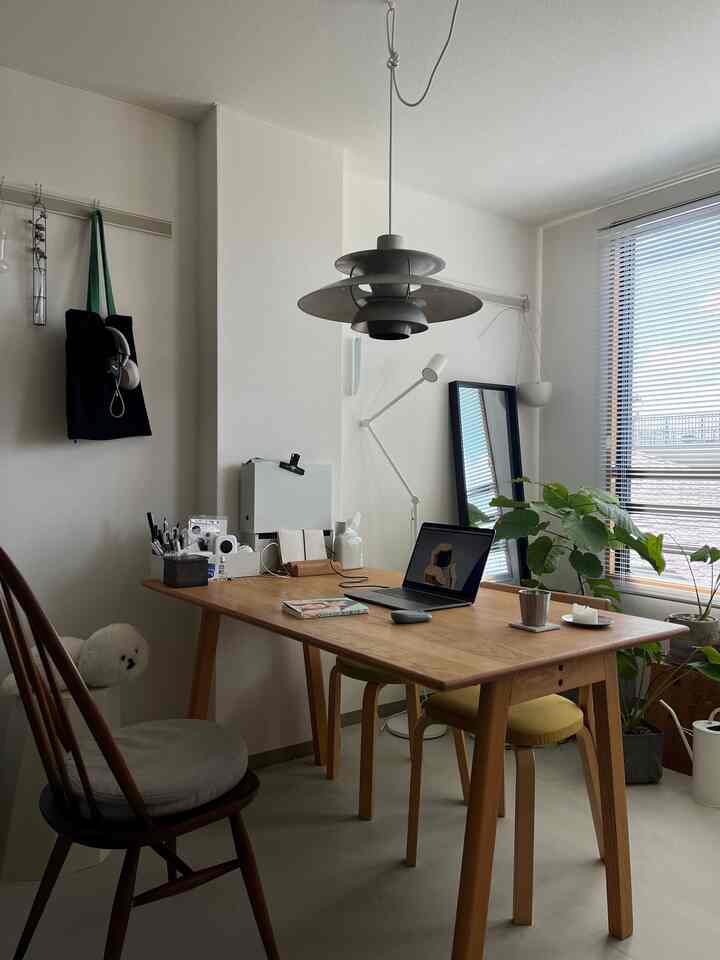 ナチュラルカラーとホワイトの1人暮らし用ホームオフィス、木製ダイニングテーブルと椅子、植物、ペンダントライトが配置された印象的な空間