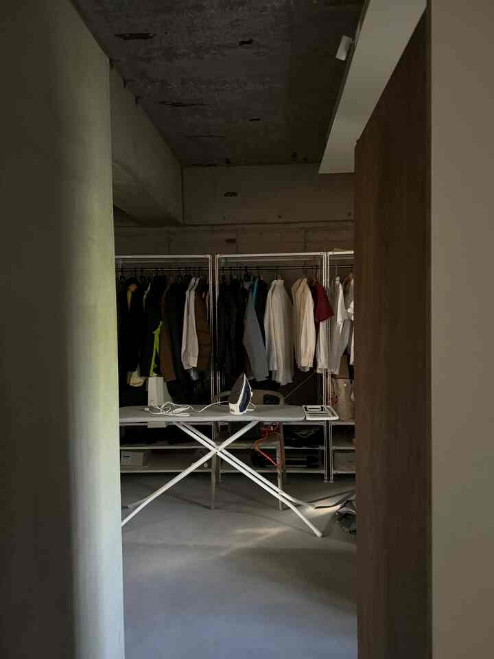 Monotone modern entrance-adjacent cloak space featuring Muji steel unit shelves and ironing board with practical ambiance