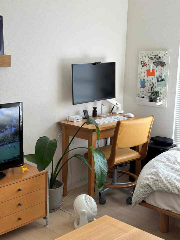 ホワイトの壁と木目調のデスクにコンピューターモニターを配したモダンなホームオフィスのある寝室